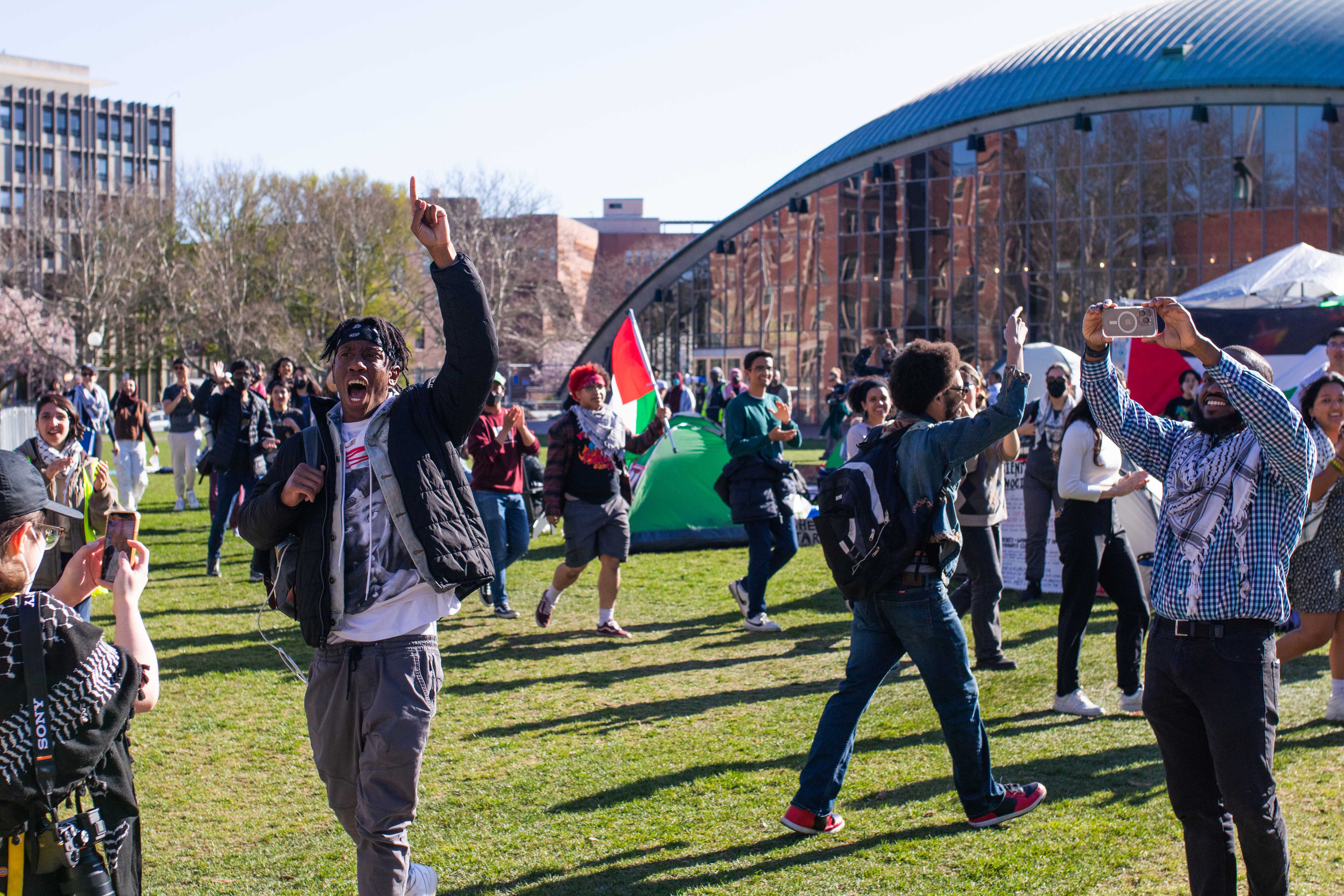 Kojo Acheampong ’26 chants at a rally outside of MIT. Nearly 50 Harvard affiliates rallied in solidarity with an MIT “Scientists Against Genocide” encampment protest. The encampment — set up by MIT affiliates Sunday evening on Kresge Lawn — consisted of at least 15 tents with Palestinian flags and cardboard signs.
