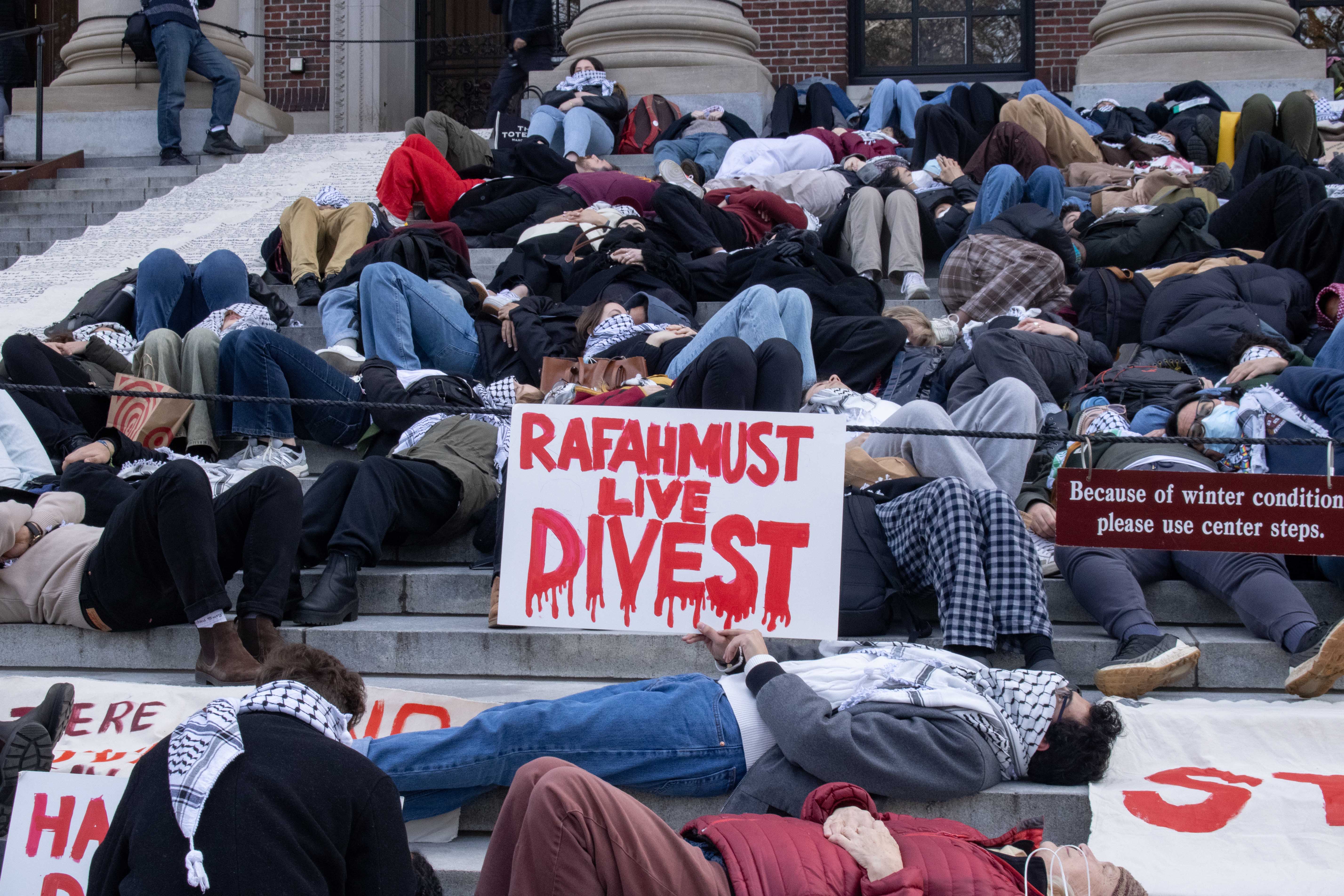 Nearly 200 students gather on the steps of Widener Library for a “die-in” demanding that Harvard disclose and divest its investments in companies with ties to Israeli settlements and the war in Gaza. After laying on the Widener steps, attendees recited Palestinian writer Refaat Alareer’s poem “If I Must Die” and played recordings of the names of individuals killed in Gaza.