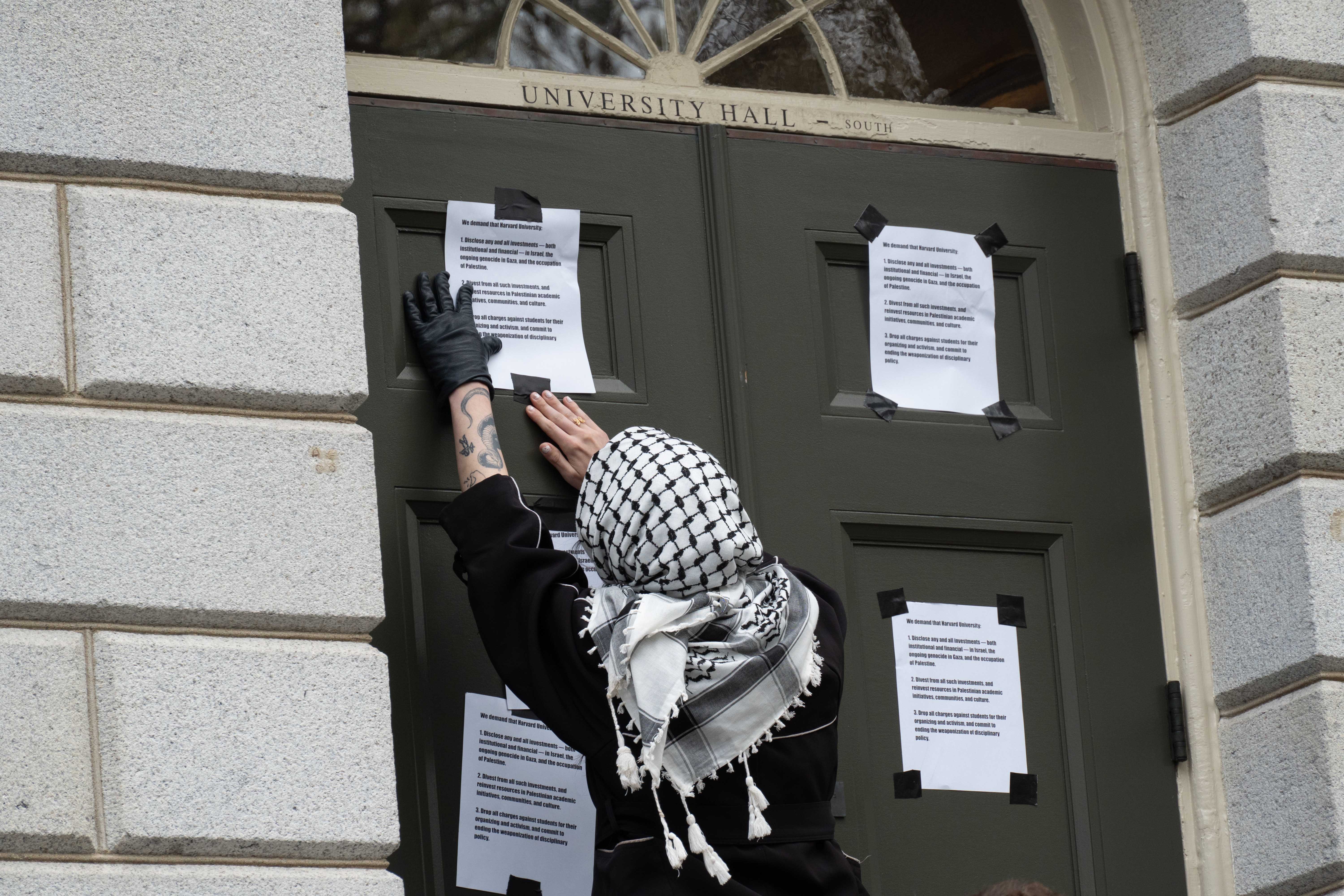 A protester tapes signs to the doors of University Hall listing the demands of Harvard Out of Occupied Palestine during a rally at the Harvard Yard encampment. More than 200 pro-Palestine demonstrators rallied for Rafah and criticized the repression of student activism at universities across the country at the protest.