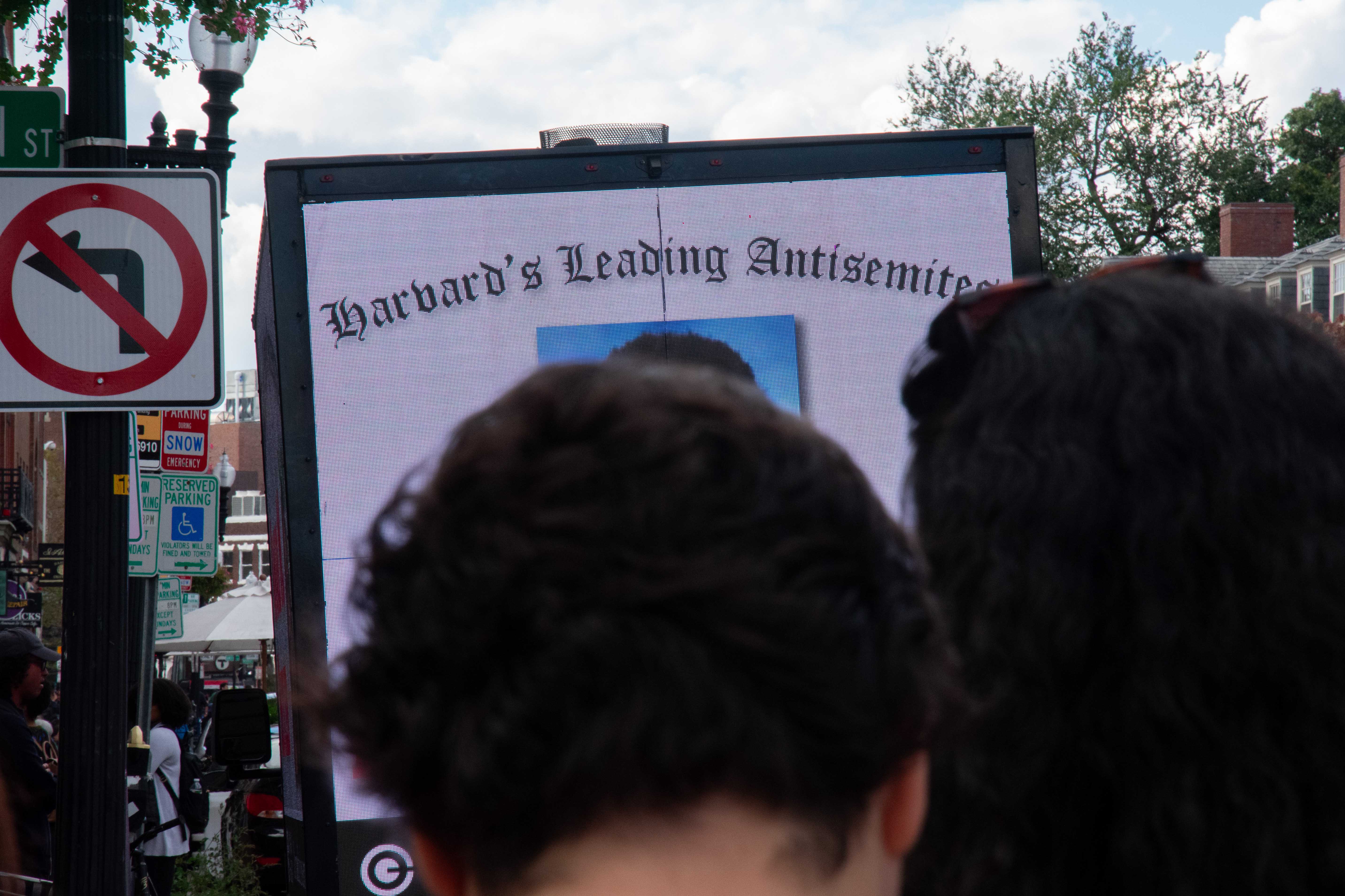 Passers-by observe a billboard truck digitally displaying the names and faces of students allegedly affiliated with student groups that signed onto a controversial statement blaming Israel for the Oct. 7 attacks.