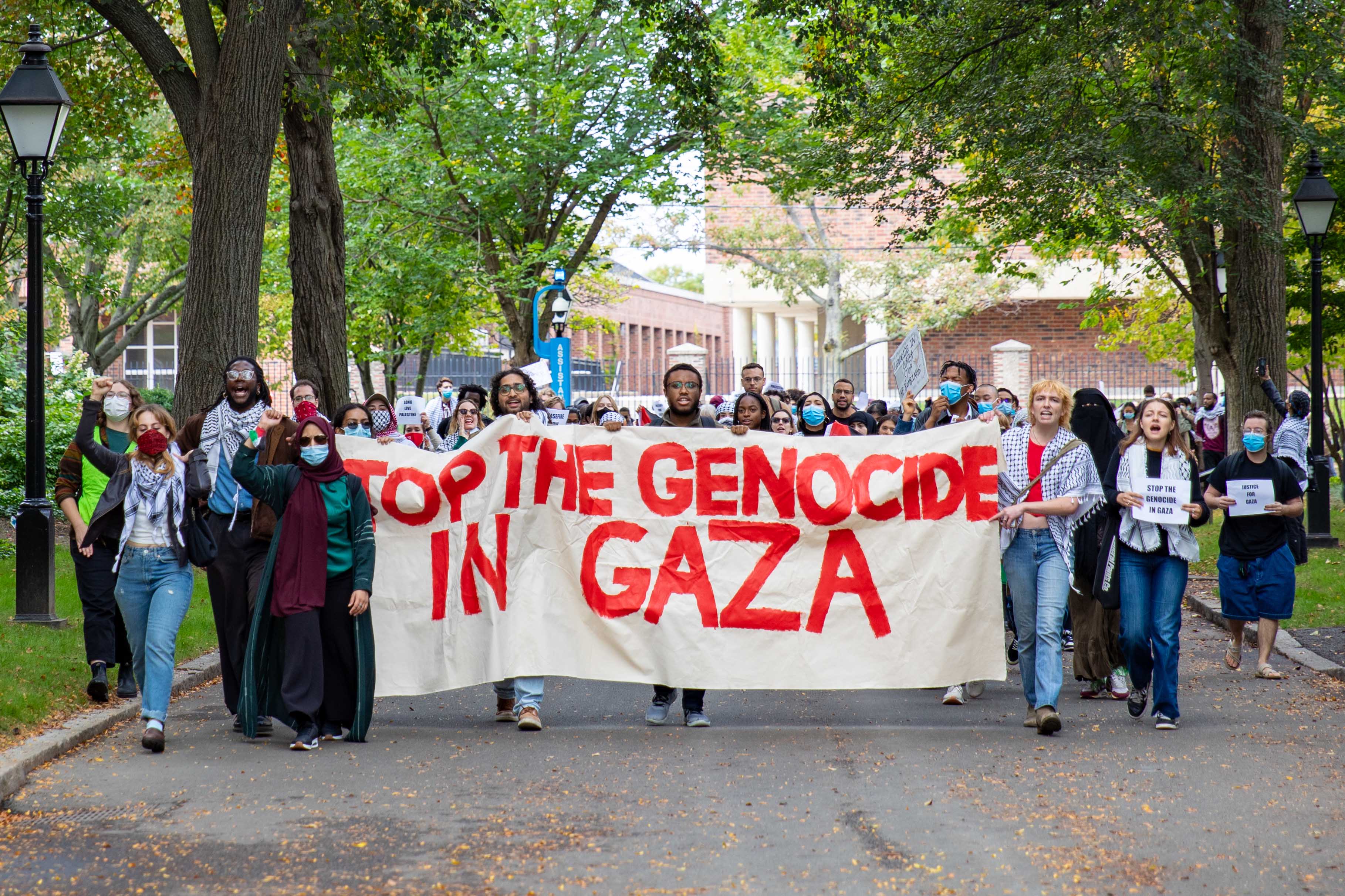 At the Business School, protesters hold up signs reading “Justice for Gaza,” “Ceasefire Now,” and “Hold Harvard Accountable For Supporting Genocide.”