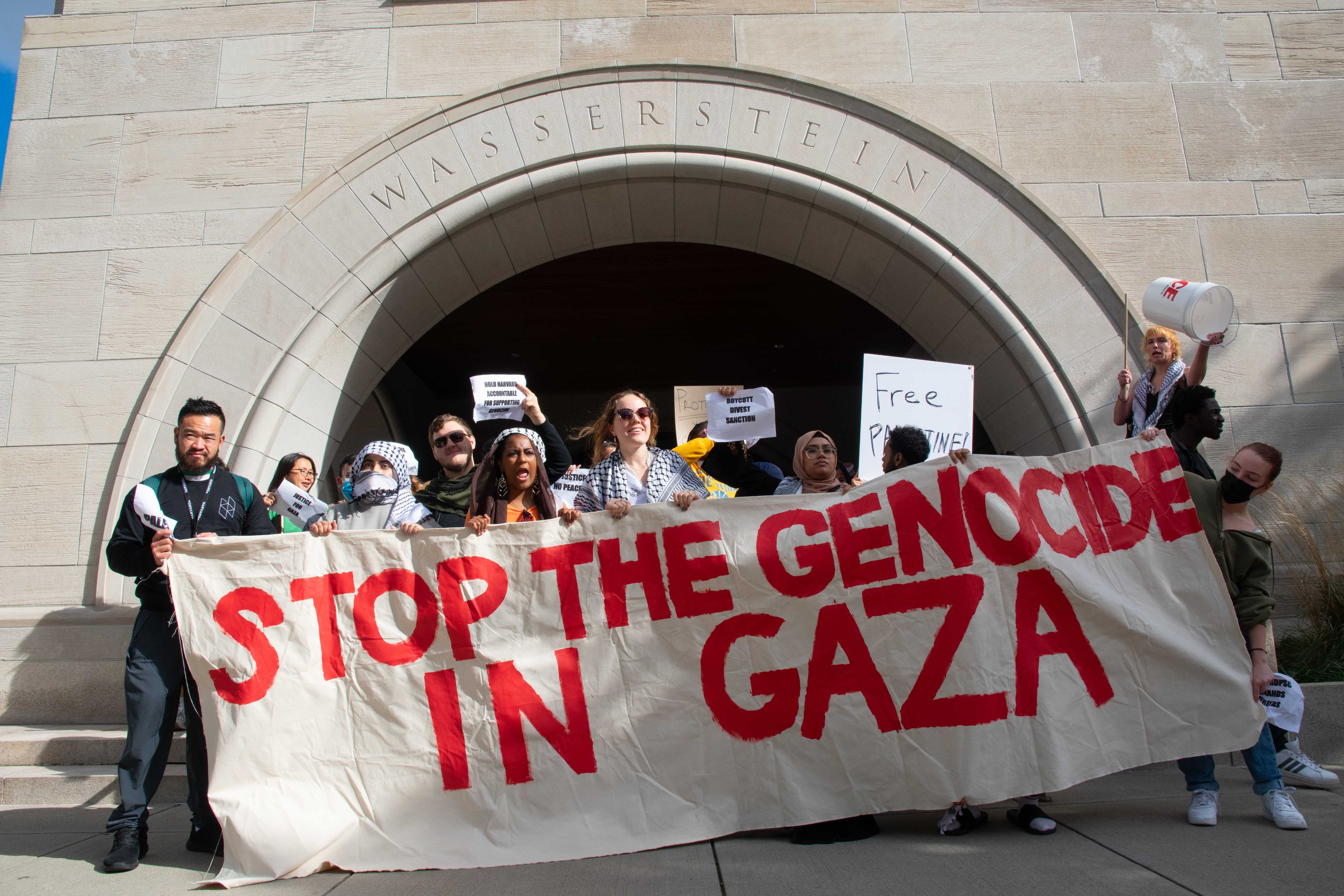 Protesters hold a banner reading “Stop the Genocide in Gaza” in front of Wasserstein Hall at Harvard Law School. Around 500 protesters supporting Palestine walked out of class and marched through multiple Harvard schools in the third protest on campus in support of Palestine following the start of the war in Israel and Gaza.