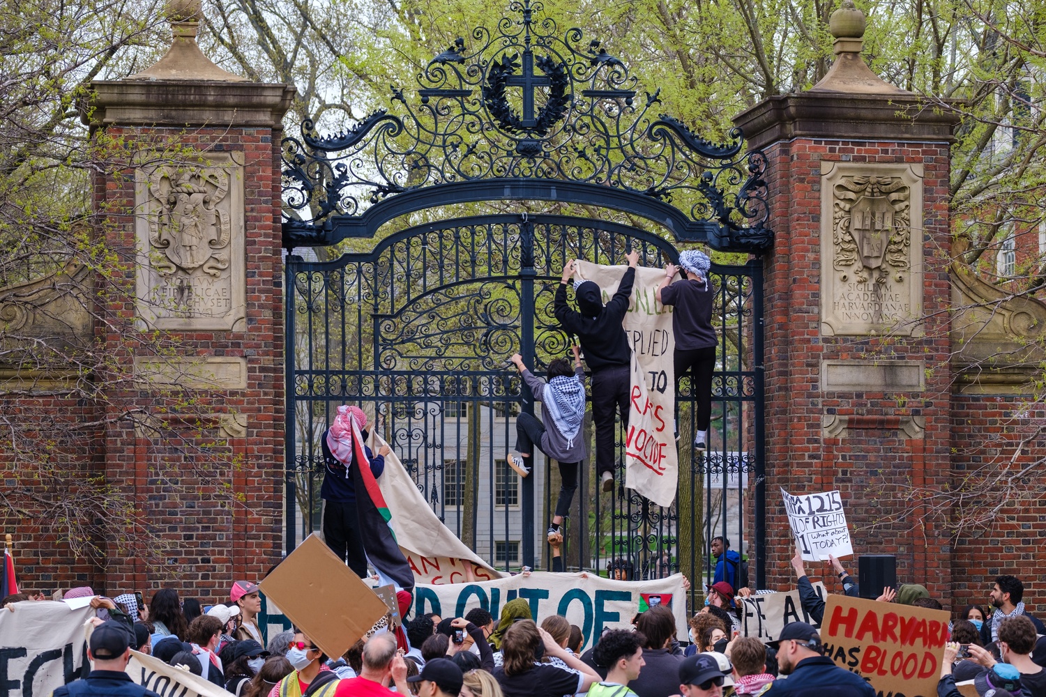 Protesters climb Johnston Gate to hang banners during a “Global Day of Action for Gaza” rally in Harvard Square. The demonstration, organized by several unrecognized student groups, accused Harvard of censoring pro-Palestine speech while resisting demands from the Trump administration.