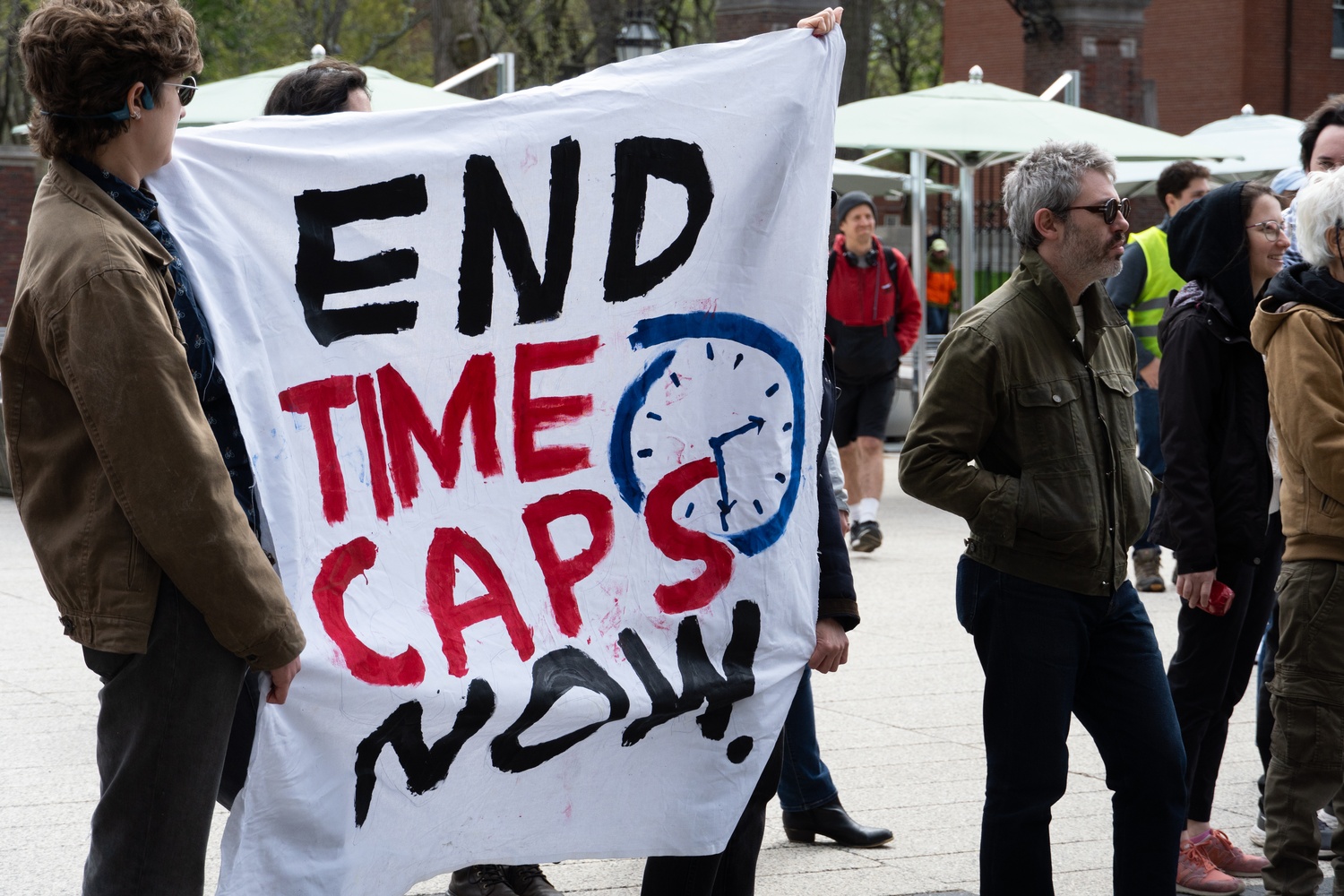 Rallygoers hold a sign calling for an end to time caps at a picket organized by campus unions in the Science Center Plaza. The rally, held during Harvard’s Visitas weekend for recently admitted students, urged the University to protect non-citizen workers and resist federal funding cuts under the Trump administration.