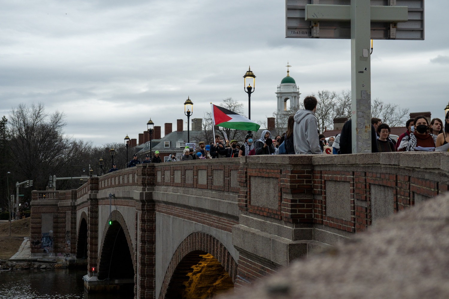 Protesters cross the Anderson Memorial Bridge during an impromptu rally led by Harvard Out of Occupied Palestine against a Harvard Israel Business Club event featuring former Israeli Prime Minister Naftali Bennett. More than 100 protesters marched in the rain from JFK Park to Harvard Business School, where they were met with barricades and a heavy security presence.